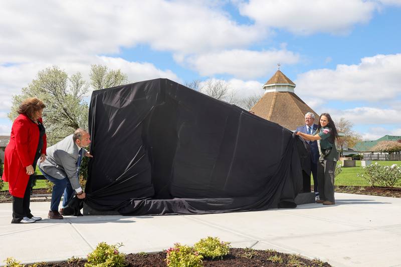 With help from her mother, Cassandra McCullough, and step father Bill Perakis, at left, and Bourbonnais Mayor Paul Schore, Alexis McCullough, right, prepares to reveal the Gold Star Families Memorial Monument during the dedication ceremony at Marcotte Park in Bourbonnais on Saturday, April 26, 2025. The project was planned and fundraised for by 17-year-old McCullough, of Bourbonnais, for her Eagle Scout project in honor of her father, Col. Mark McCullough.