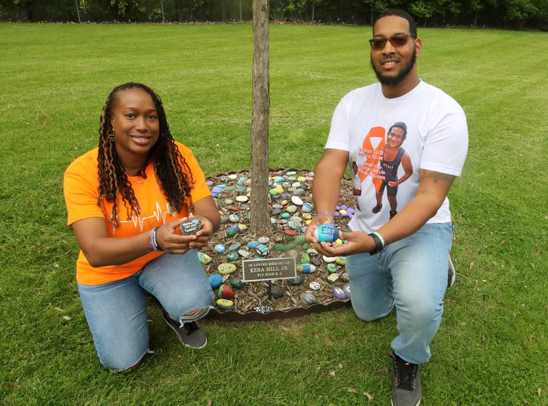 Andrea Elion, mother of Ezra Hill Jr. and Brandon Elion Ezra’s stepfather, kneel beside a tree and rock garden at Tyler Elementary School Monday, May 12, 2025, that is dedicated to the memory of Ezra, who was was murdered in 2019 in Harvey. An Ezra Hill Jr. Memorial Rock Painting event will be held on June 7 at the school in DeKalb.