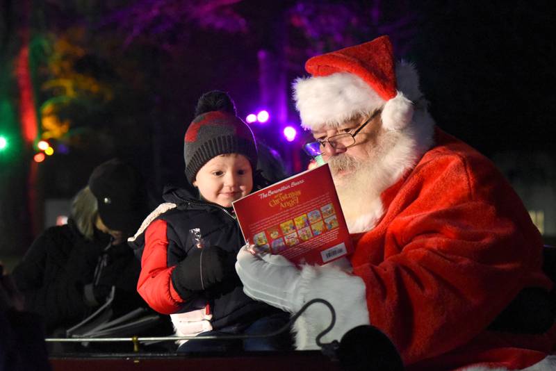 Three-year-old Ellis Fry smiles as he looks at a book with Santa during Christmas in the Village on Saturday, Dec. 2, 2023 in Mt. Morris.