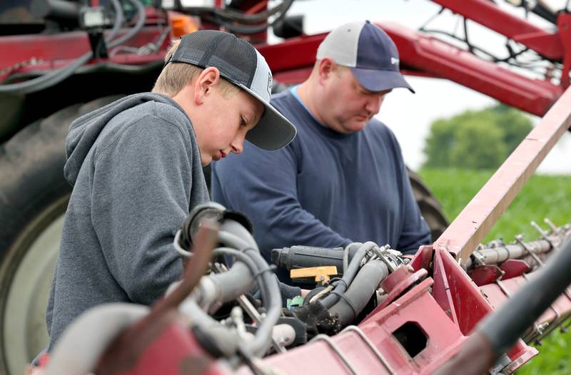 Farmer Mike Schweitzer and his son Eli, 12, change the sprayer nozzles on a tractor in one of his fields Friday, June 16, 2023, on his farm in Malta.