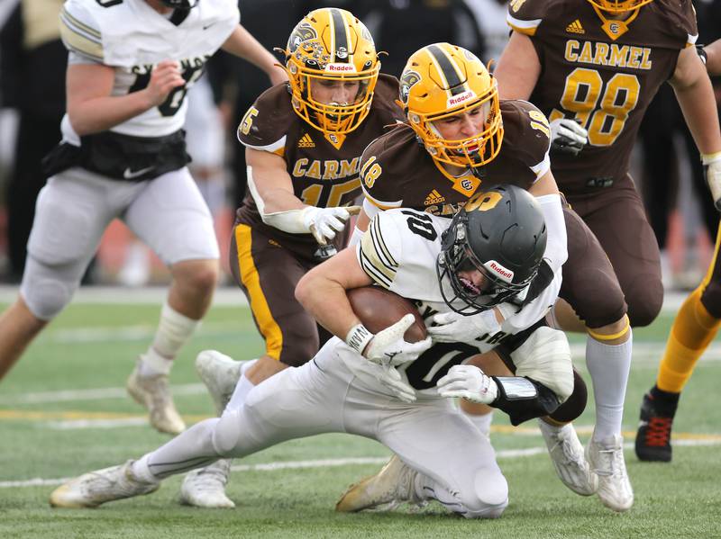 Sycamore's Zack Crawford is brought down by Carmel's Kyle Lynch (left) and Ryan Harris during their Class 5A second round playoff game Saturday, Nov. 5, 2022, at Carmel Catholic High School in Mundelein.