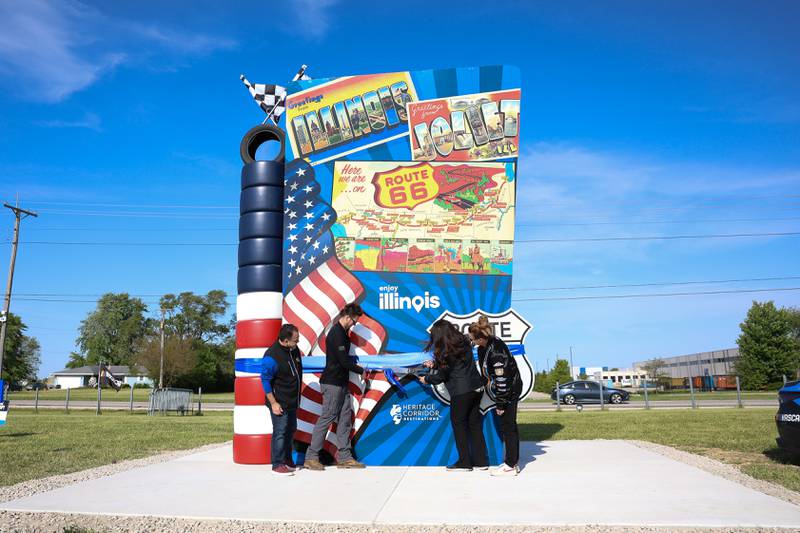 Artist Tim Harmon, second from left, cuts the ceremonial ribbon at the unveiling of the new Route 66 sculpture along South Chicago Street at the Route 66 Raceway on Tuesday, May 12, 2026 in Joliet.
