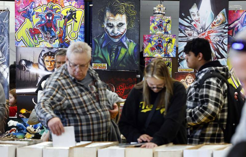 People look through comics as the art of Beth Zwolski Tobias “The Chalk Girl” looks over them during the DuPage Comic Con Saturday, March 22, 2025 at the the DuPage County Fairgrounds in Wheaton Ill.