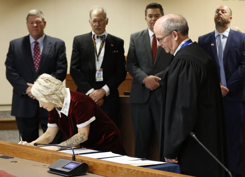 New McHenry County Board member Deena Krieger, R-Island Lake, signs the oath of office on Monday, Dec. 2, 2024, at the McHenry County Administration Building in Woodstock. In the background, from left to right: Board members Jim Kearns, R-Huntley, Carl Kamienski, R-Johnsburg, Mike "Shorty" Shorten, R-Crystal Lake, Paul Thomas, R-Wonder Lake and Chief Judge Michael Feetterer.