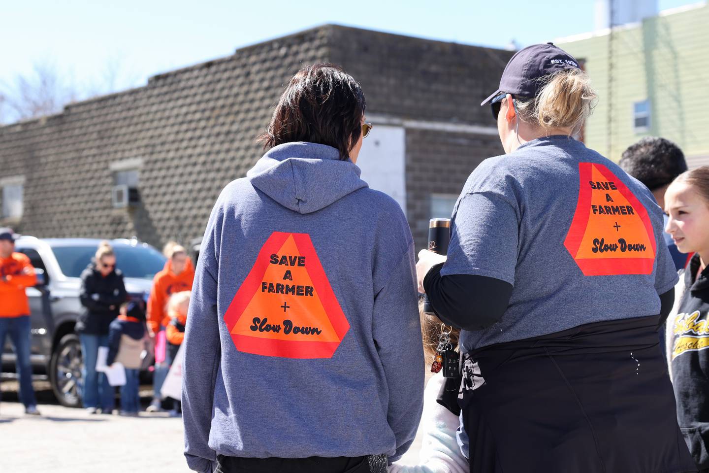 Shirts and hoodies sharing the message "Save a Farmer and Slow Down' are worn as dozens line Main Street in Cabery to welcome home Willy VanWassenhove, a Cabery farmer that was seriously injured on Sept. 20, as he arrives back to the area on Saturday, March 22, 2025.