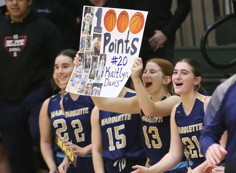 Marquette players (from left) Madisyn Trainor, Emily Ryan-Adair, Lucy McGrath and Kinley Rick hold a sign celebrating teammate Kaitlyn Davis making 1,000 career points against Amboy/Ohio during the Class 1A Regional championship on Thursday, Feb. 20, 2025 at St. Bede Academy.