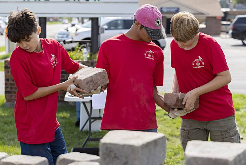 Troop members Ayden Arnold, left, 11, Cruz Ocampo, 16, and Ethan Boss, 15, form a human chain to move bricks into place Saturday, Sept. 23, 2023.