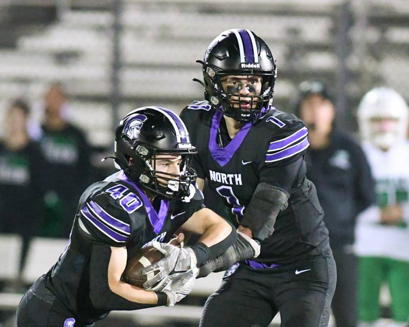 Downers Grove North's Owen Lansu, right, hands the ball off to teammate a teammate during the game on Friday Oct. 10, 2025, while taking on York High School held at Downers Grove North High School.