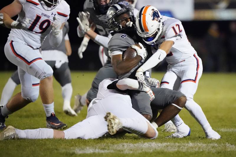 Oswego East's Jasiah Watson (2) is hit by Oswego’s Easton Ruby (left) and Mariano Velasco (12) during a football game at Oswego East High School on Friday, October 25, 2024.