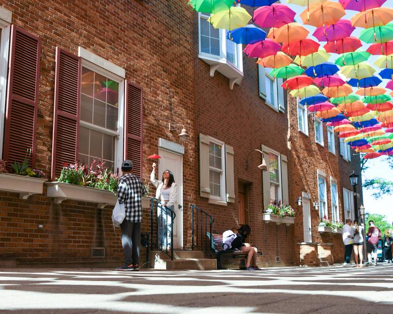 Kyle Long, left, takes a photograph of his friend Ling Chen of Clarendon Hills under the umbrellas at Schiller Court on Saturday May 31, 2025, during the Elmhurst Summer Kick Off Party held at City Centre Fountain Plaza in Elmhurst.