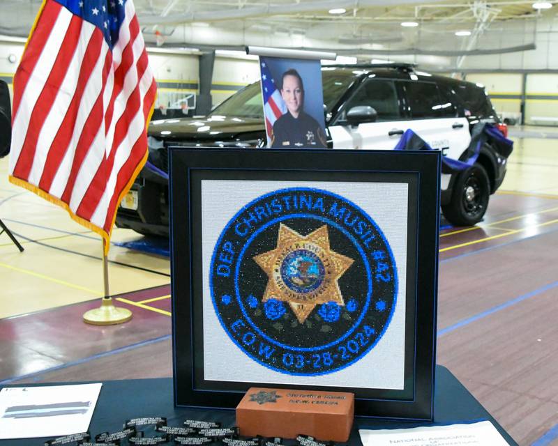 Items are displayed on a table to remember the late DeKalb County sheriff's deputy Christina Musil (shown), 35, during a memorial vigil on Saturday, March 29, 2025, held at the Sycamore High School Field House. Musil was killed in the line of duty in a rear-end car crash in Waterman while on patrol on March 28, 2024.