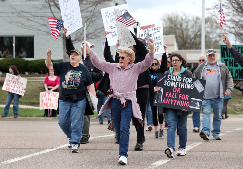 Protesters cross Sycamore Road Saturday, April 19, 2025, during a “No Kings” rally and march at Hopkins Park in DeKalb. The group was protesting what they’ve argued is the unlawful and harmful federal policies of President Donald Trump and his administration.