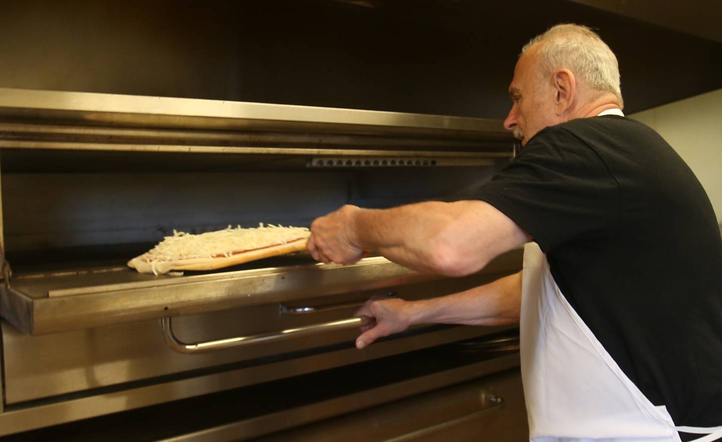 Joe Evola, owner of Sam's Pizza, places a pizza in the oven on Wednesday, June 4, 2025, at his restaurant in Marseilles.  Sam's Pizza celebrates its 50th anniversary in business this year.