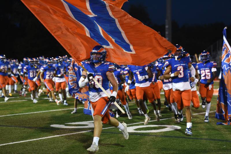 Hoffman Estates’ Anthony Elenz carries the school’s flag as the Hawks run onto the field prior to during Friday’s home football game against Maine East.