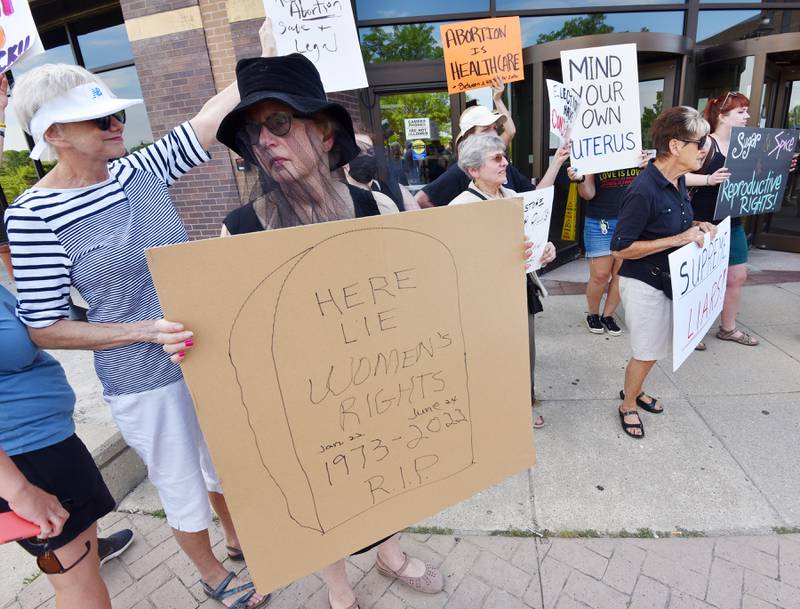 Susan Becker, of Downers Grove wears a black funeral veil and holds a sign reading “Here lie women’s rights Jan 22, 1973-June 24, 2022 R.I.P.” at a rally at the Henry J. Hyde Judicial Office Facility in Wheaton. About 140 people rallied in support of women’s fundamental right to privacy and bodily autonomy on Friday, June 24, 2022.