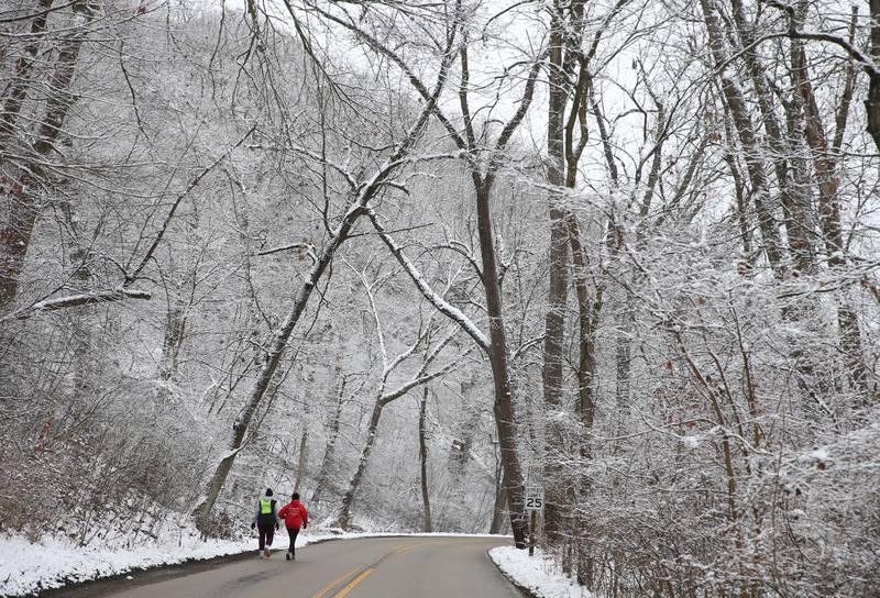 Runners jog on the main-entrance road to Starved Rock State Park as snow covers the trees on Sunday, Jan. 7, 2024.