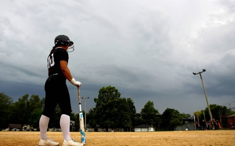 Prairie Ridge’s Emily Harlow waits for a verdict on game play as umpires and coaches meet at home plate to discuss the weather while a storm rolls in for Prairie Ridge and Harvard’s game in Class 3A softball regional final action at Lions Park in Harvard Friday.