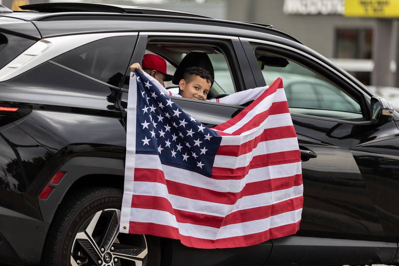 A young passenger holds an American flag while passing by the No Kings Protest at Mall Loop Drive in Joliet on Oct. 18, 2025.