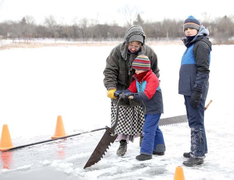 Tonya Mattson helps Wyn Perdue, 6, of Naperville to saw out blocks of ice from Timber Lake at Kline Creek Farm as Elliott Perdue, 11, looks on during the harvest ice on Friday, Jan. 24 2025 in West Chicago.