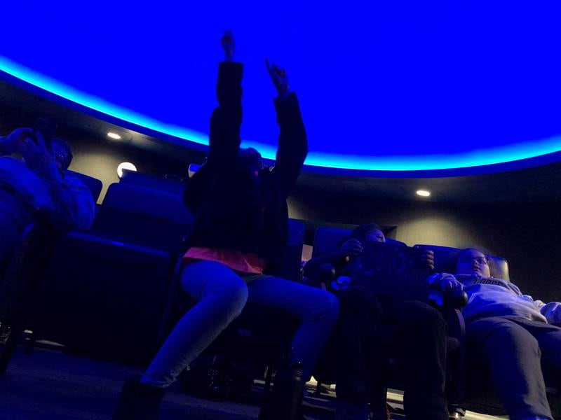 Kelly (armed raised), Estela and Kendall Merkel wait for the "Eclipses of the Sun" show to start Friday, April 5, at McHenry County College's Planetarium, ahead of the April 8 solar eclipse.