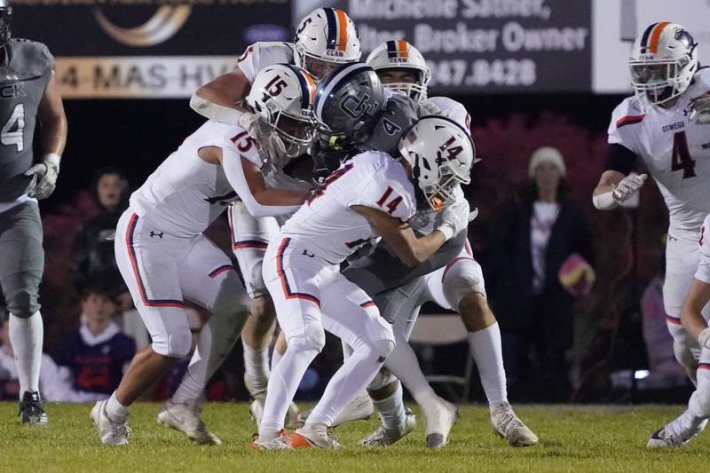 Oswego East's Lincoln Ijams (4) is hit by four Oswego defenders during a football game at Oswego East High School on Friday, October 25, 2024.