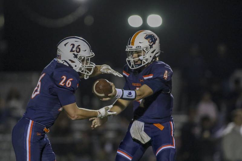 Oswego's Drew Kleinhans (4) hands off to Dekker Zelensek (26) during football game between Oswego East at Oswego Friday, Oct 17, 2025 in Oswego.