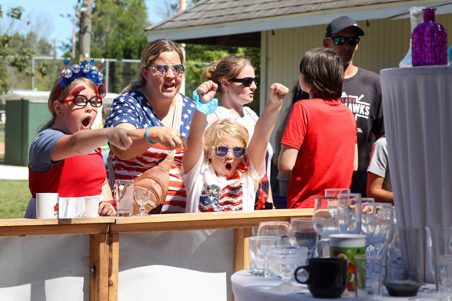 Elaina Pena, 8, right, celebrates throwing a dime into a glass as her sister, Sophia, 9, left, and mother Crystal, all of Manteno, play the Herscher FFA dime toss during the 104th annual Herscher Labor Day Celebration on Monday, Sept. 1, 2025.