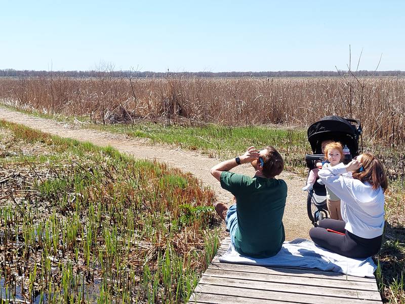 (Left) Ben Fogle, of Cedar Point, and his wife Macy watch the partial solar eclipse from the boardwalk of the Dixon Waterfowl Refuge outside of Hennepin with their daughters Vada and Indie.