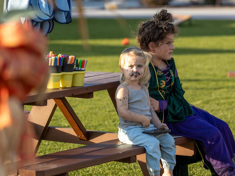 (from left) Oakley Baker and Vivian Carlson sit on a bench at the annual Witches Walk on Friday, Oct. 17, 2025, at the Market on Mill in Utica.