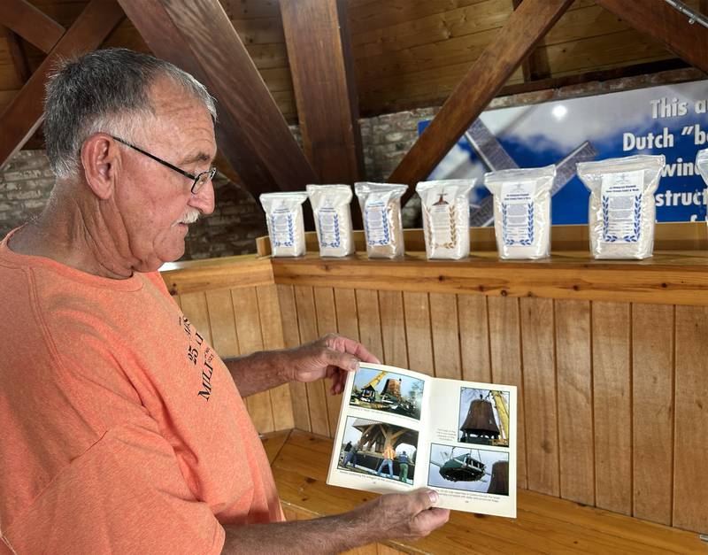 Dale Green, a volunteer miller for de Immigrant windmill in Fulton, shows one of the books that chronicles the construction of the authentic Dutch windmill, during the 25th anniversary celebration on Saturday, June 7, 2025. Displayed on the shelf are bags of flour, ground at the windmill, that are available for purchase at the Windmill Cultural Center, located across the street from the windmill.