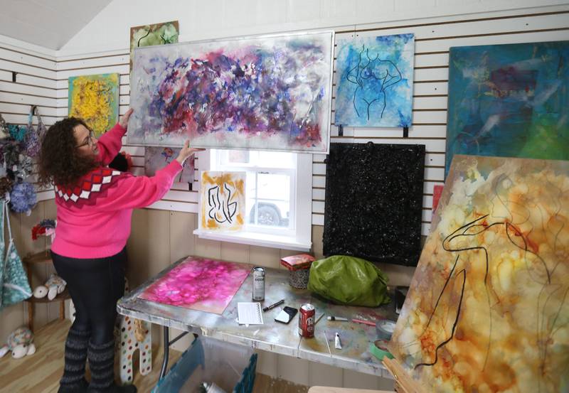Lisa Marie, hair stylist and abstract artist, hangs one of her fire paintings inside a hut on Saturday, Feb. 8, 2025 at the Market On Mill plaza in Utica. Marie painted items and sold them at the Winter Wine Walk.