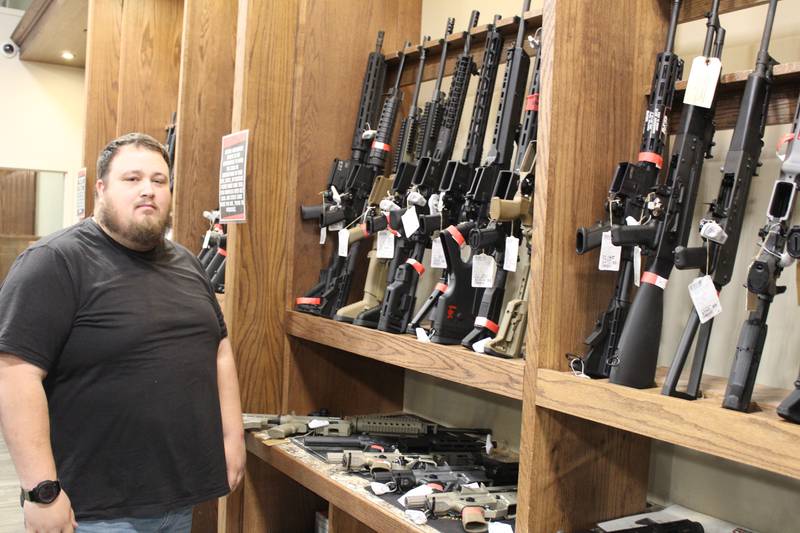 Second Amendment Sports Director of Marketing and Public Relations Tyler Duncan stands next to firearms banned by the Protect Illinois Communities Act that passed earlier this year.