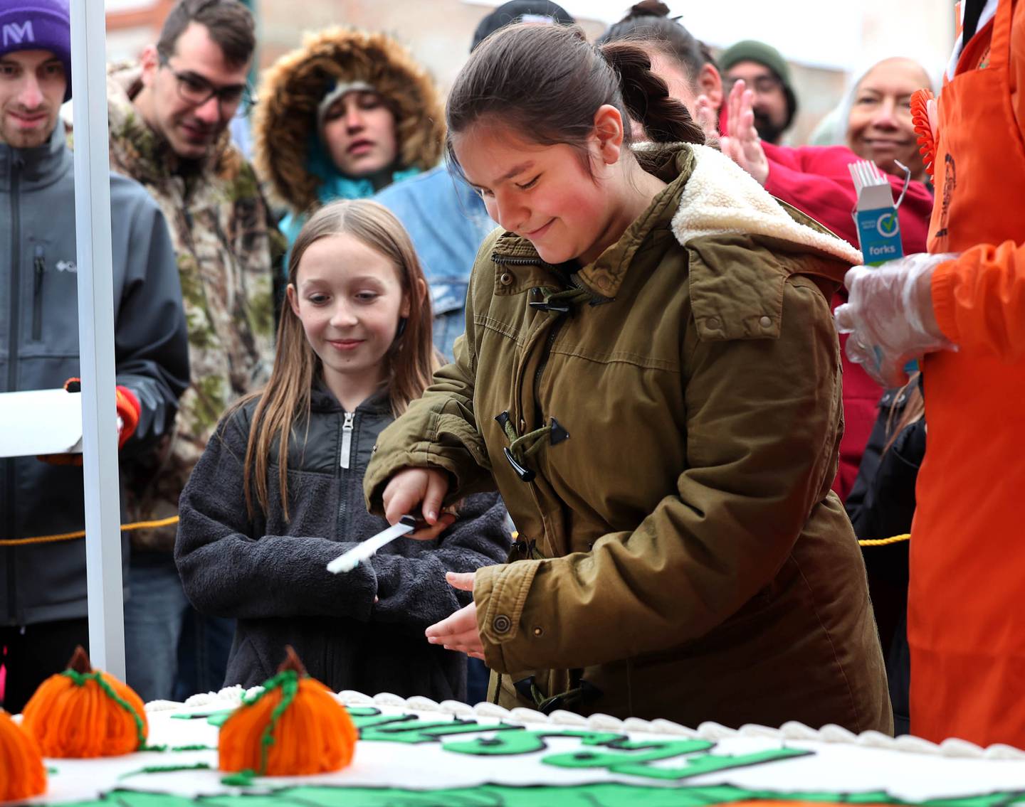 Rayven Rosas, (right) this year’s theme winner, makes the first cut of the cake as honorable mention winner Annabelle Hochstatter waits for her turn Wednesday, Oct. 22, 2025, during opening day of the Sycamore Pumpkin Festival.