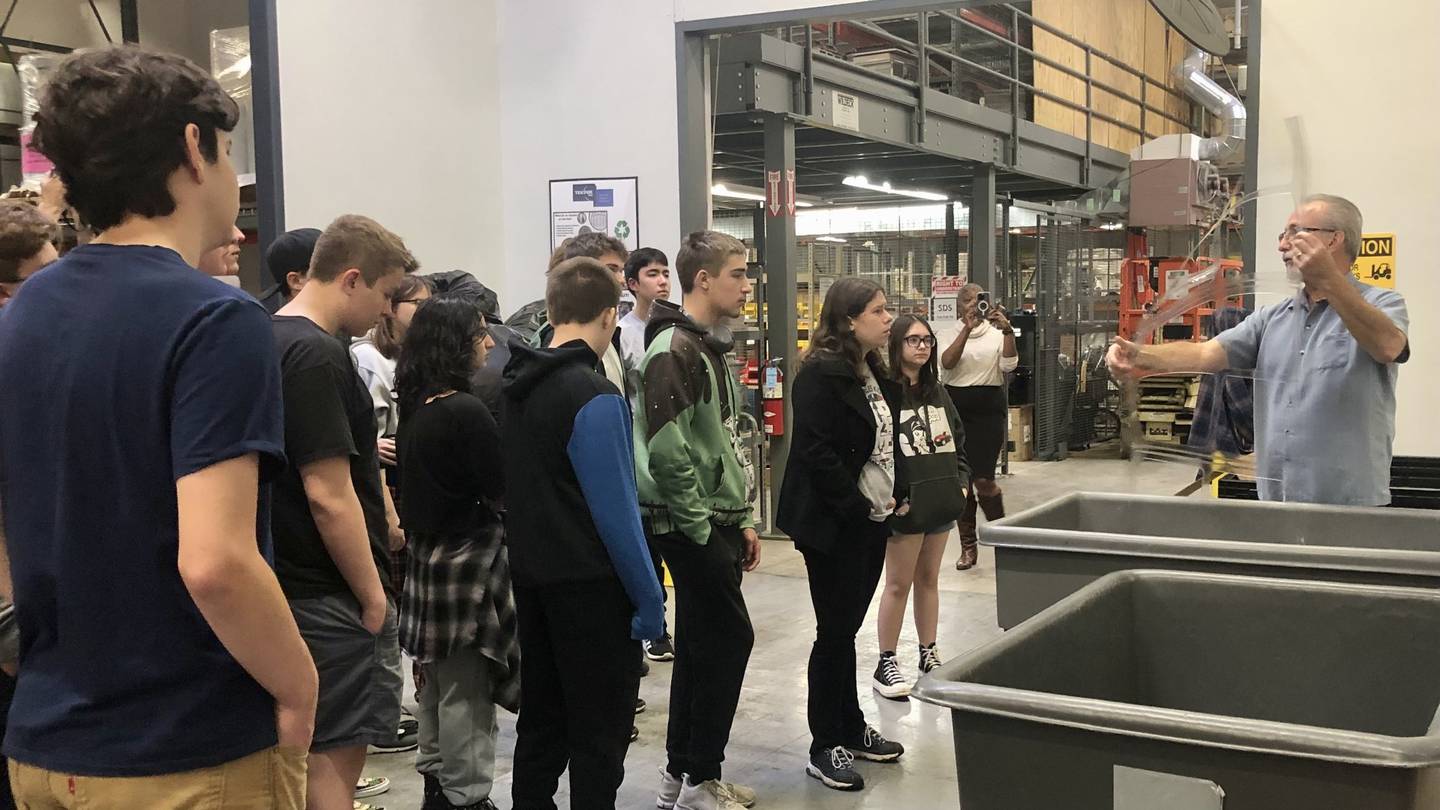 Tek Pak senior manufacturing engineer Pat Conley (right) shows School District 303 students the plastic bindings used in the factory's processes, which are recyclable and will be reused for work in the future, during a tour of the factory in St. Charles  on Oct. 25, 2023.