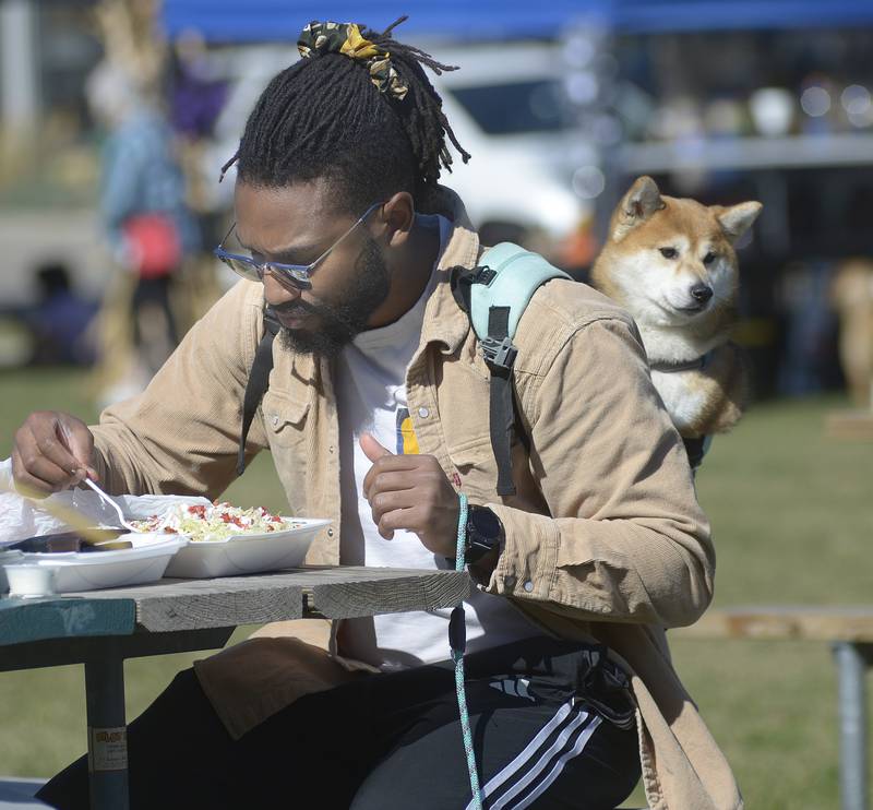 Ajani Crosley enjoys a meal while his dog Icarus rests comfortably on his back Sunday, Oct. 6, 2024, during the annual Bill’s Barktoberfest on the Jordan block in Ottawa.