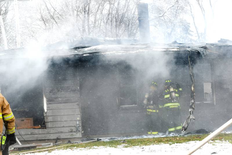 Oregon firefighters examine the charred remains of a home in Byron after several area fire departments battled the fire at 115 W. Third Street Saturday morning. One woman was declared dead after being found outside the home after a power line fell on the house causing to become "electrified," a fire official said.