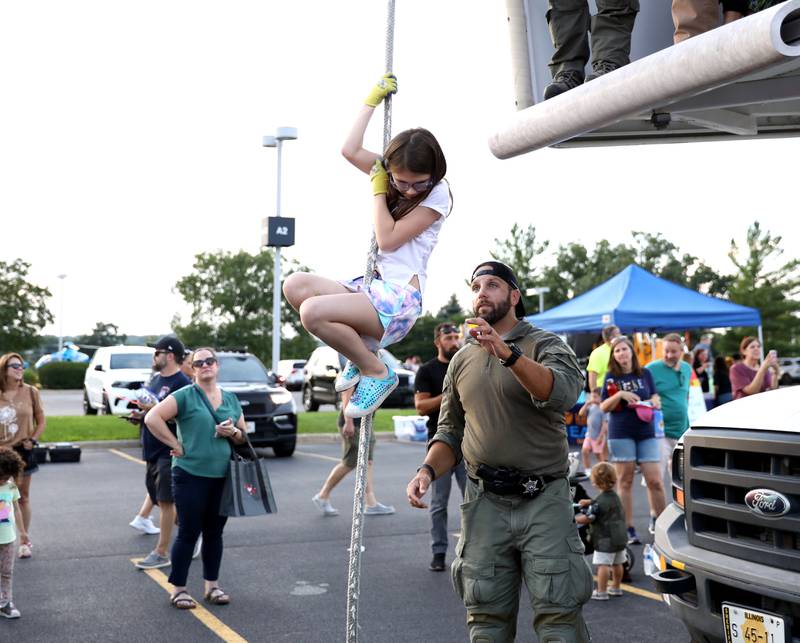 Emily Darger, 8, of Batavia is helped down by Kane County Sheriff SWAT member Joe Gaske during the Kane County Sheriff’s Office National Night Out event in St. Charles on Tuesday, Aug. 1, 2023. The community-building event began nationally in 1984.