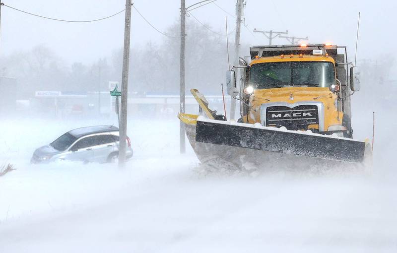 A snowplow travels by a vehicle in the ditch Monday, March 16, 2026, at the corner of Somonauk Road and Fairview Drive in Cortland. A March snowfall covered DeKalb County in about six inches of the white stuff Sunday night into Monday.
