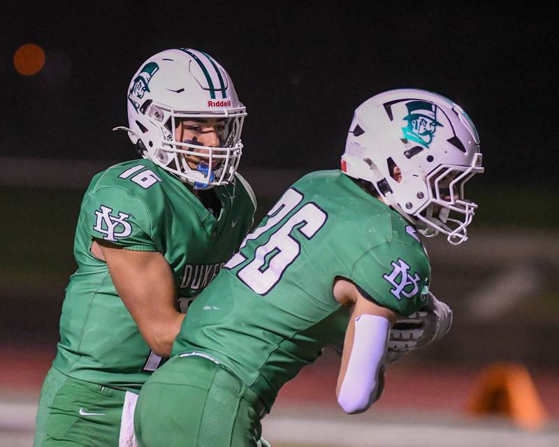 York's Zack Assaad (16) hands the ball off to teammate Henry Duda (26) during the game on Friday Oct. 17, 2025, while taking on Glenbard West held at York High School.