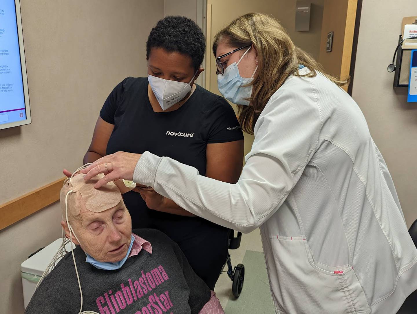 La Keysha James, a device support specialist with Novocure, assists Joan Quaresima, a radiation oncology nurse at Joliet Oncology-Hematology Associates, with the application of transducer arrays to the scalp of Libby Hall, 75, of Joliet, on Friday, Sept. 16, 2022. . Hall was diagnosed with glioblastoma multiform, an aggressive brain cancer, in 2020 and is currently wearing a device called Optune, which delivers an electrical field into the cancer cells in her brain.