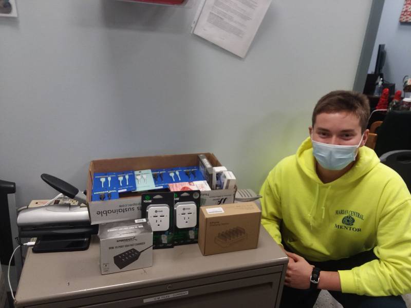 Matthew Cotting, a senior at Marian Central Catholic High School, sits next to a box of chargers and other technology the business club helped donate to McHenry PADS.