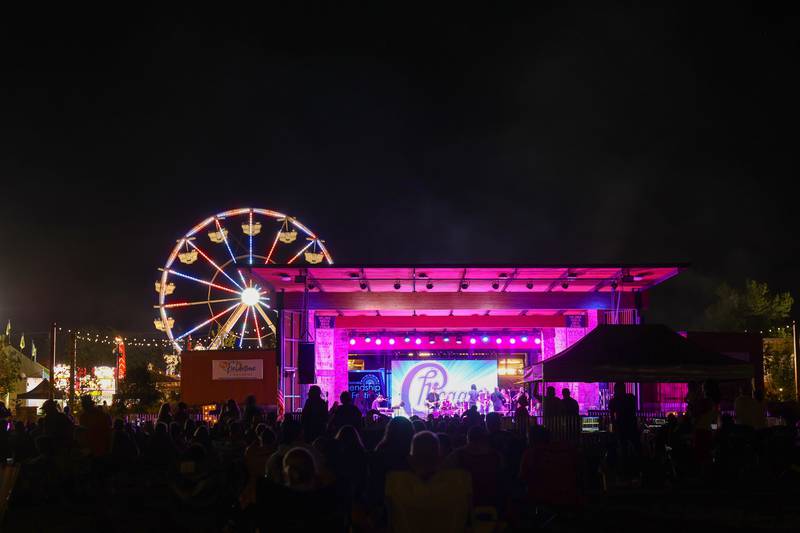 Festivalgoers enjoy live music by the Chicago Tribute Anthology as the ferris wheel glows behind the stage at The Grove during the 50th Bourbonnais Friendship Festival on Saturday, June 28, 2025.