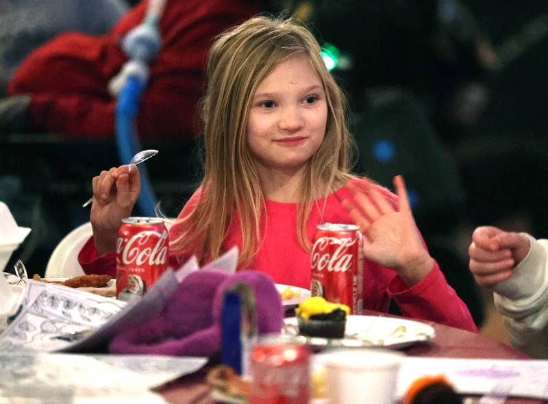 Leah Haynes, 8, from Sycamore, waves at another table between bites Wednesday, Nov. 26, 2025, during A World of Thanks, Community Thanksgiving hosted by DeKalb Mutual Aid at the McCabe’s building in DeKalb.