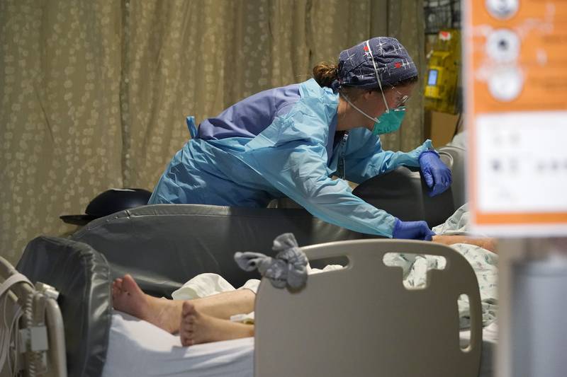 Registered nurse Estella Wilmarth tends to a patient in the acute care unit of Harborview Medical Center, Friday, Jan. 14, 2022, in Seattle. Washington Gov. Jay Inslee is deploying 100 members of the state National Guard to hospitals across the state amid staff shortages due to an omicron-fueled spike in COVID-19 hospitalizations. Inslee announced Thursday that teams will be deployed to assist four overcrowded emergency departments at hospitals in Everett, Yakima, Wenatchee and Spokane, and that testing teams will be based at hospitals in Olympia, Richland, Seattle and Tacoma. (AP Photo/Elaine Thompson)