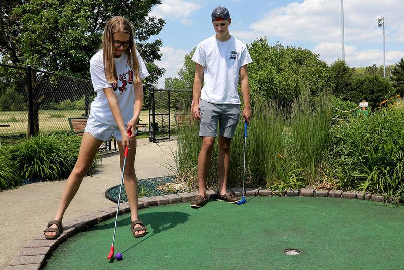 Julia Pietrzyk, left, and Connor Herrmann, both 18 and from Cary, take turns putting on the 18th hold during a tied game of mini golf at the Lippold Park Family Golf Center on Wednesday, June 17, 2020 at Lippold Park in Crystal Lake.  The miniature golf course reopened Monday and does not require customers to wear face masks, however staff varies the courses assigned to customers so that they remain more socially distant from one another.