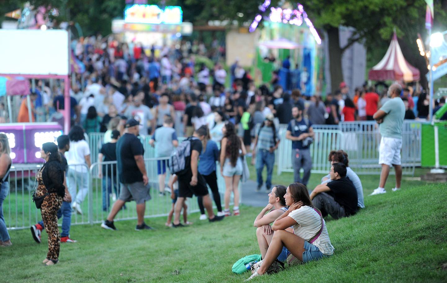 Fair goers relax on the lawn and watch the crowds pack the amusements during the 83rd Montgomery Fest on Saturday, Aug. 19, 2023.