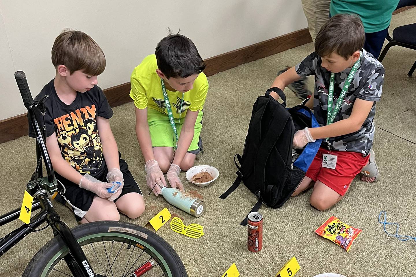 AJ McNeeley (pictured left to right), Nashten Funderberg and Nicholas Klinefelter examine evidence and dust for fingerprints of a mock crime scene during the final day of 4-H Crime and Spy camp.