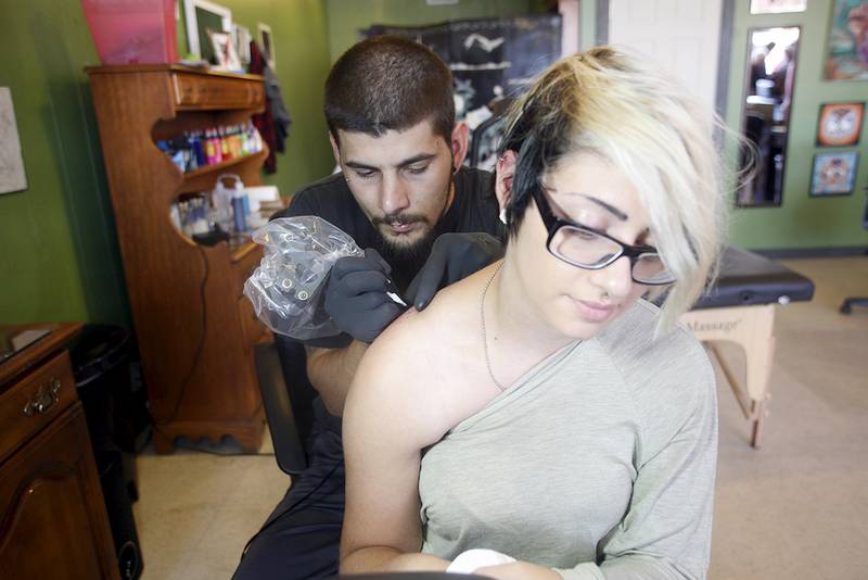 Edwin Patterson tattoos the shoulder of Kaytlynn Crowe of DeKalb.