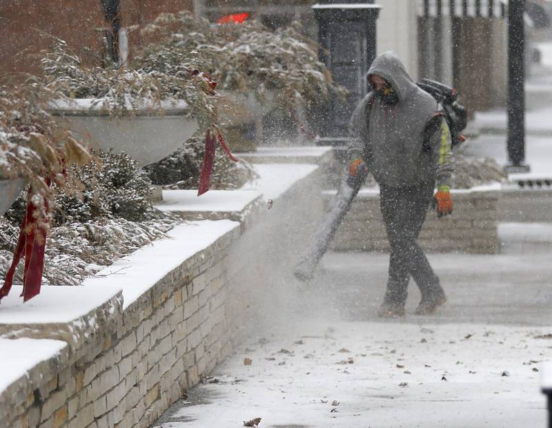 A man uses a blower to blow snow of a sidewalk on Feb. 12, 2025, in downtown Crystal Lake as a winter storm starts to bring heavy snow to the McHenry County area