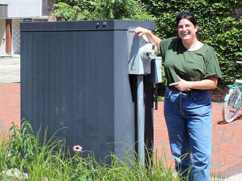 DeKalb Citizens’ Community Enhancement Commission Member Jeanine Holcomb standing next to a utility box in Van Buer Plaza that is one of three utility boxes in downtown DeKalb selected to be used for a new public arts initiative.